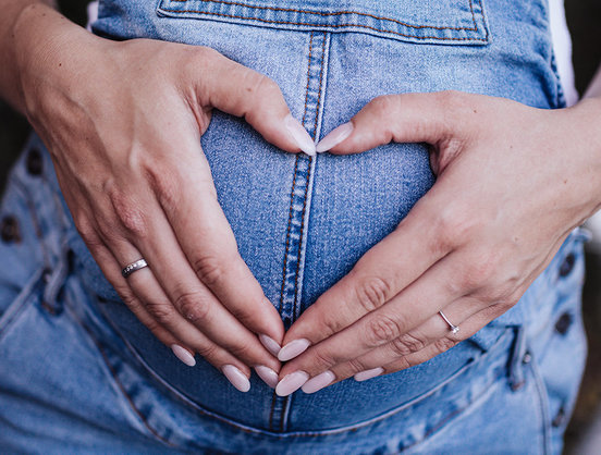 Schwangere formt mit ihren Händen ein Herz auf dem Babybauch