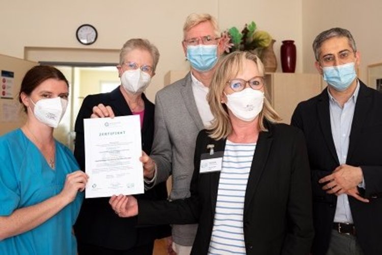 Das Gruppenbild zeigt fünf Personen bei der Übergabe des Zertifikats von Frau KAtja Rothe (GeriZert) an das Team der Geriatrie